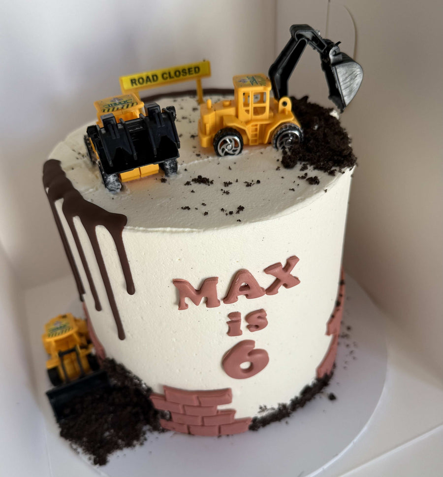 Construction-themed birthday cake with toy trucks and 'MAX is 6' text on a white background.