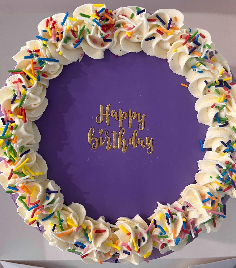 Close-up of the gold luster dust 'Happy Birthday' message on a fondant topper, atop a colorful cake, perfect for a memorable birthday celebration