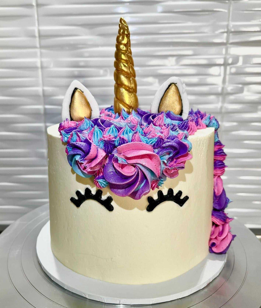 Unicorn Cake Brisbane, Close-up of a unicorn cake decorated with vibrant purple, pink, and blue icing, featuring a golden fondant horn and delicate fondant ears, perfect for a magical birthday celebration.