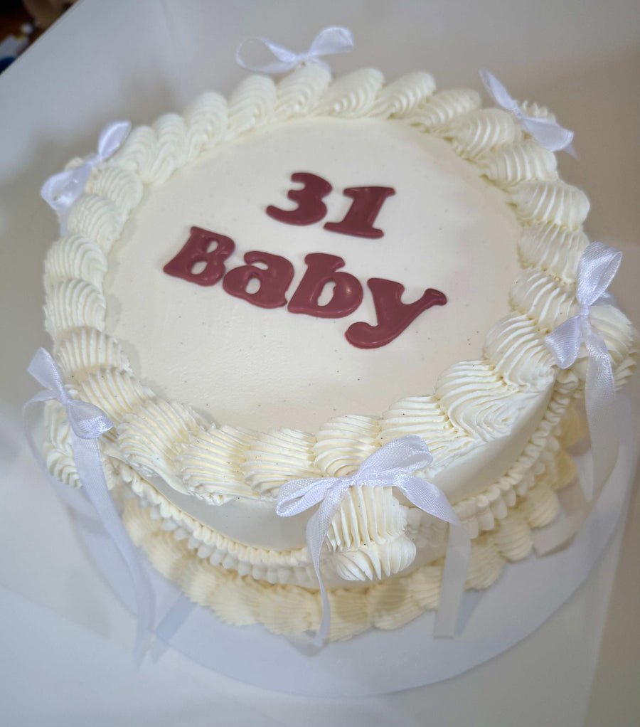 White cake with '31 Baby' text and white ribbons on a white background