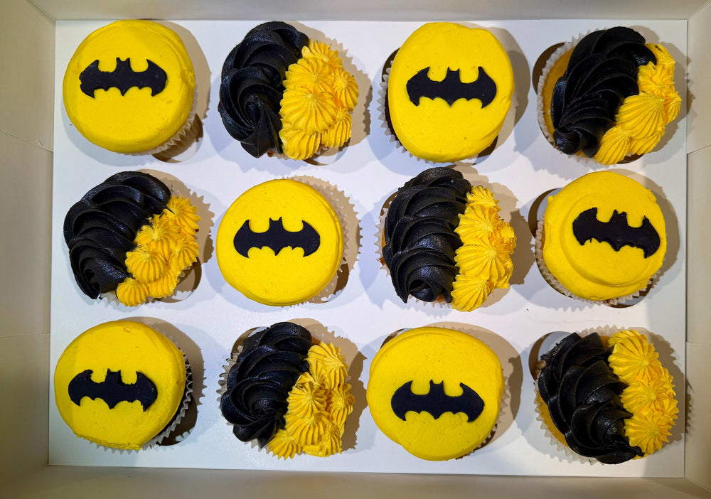 Box of cupcakes with yellow and black icing in the shape of Batman logos.