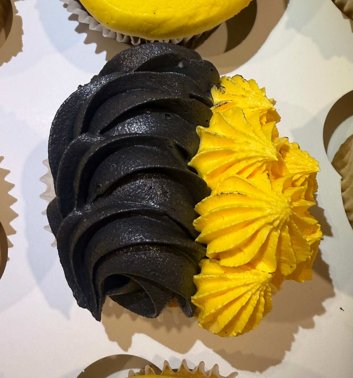 Two cupcakes with black and yellow frosting on a white surface.