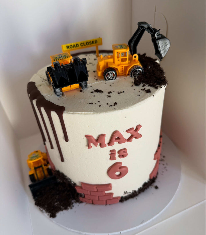 Construction-themed birthday cake with toy vehicles and 'MAX is 6' text on a white background