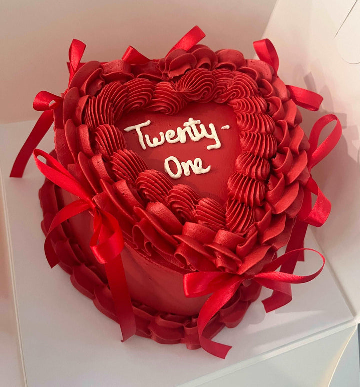 Beautifully decorated heart-shaped vintage cake, featuring delicate hand-piping and bows, ideal for heartfelt celebrations.