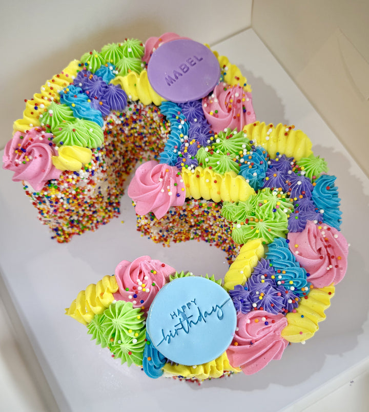 Colorful birthday cake shaped like the number '3' with frosting and sprinkles.