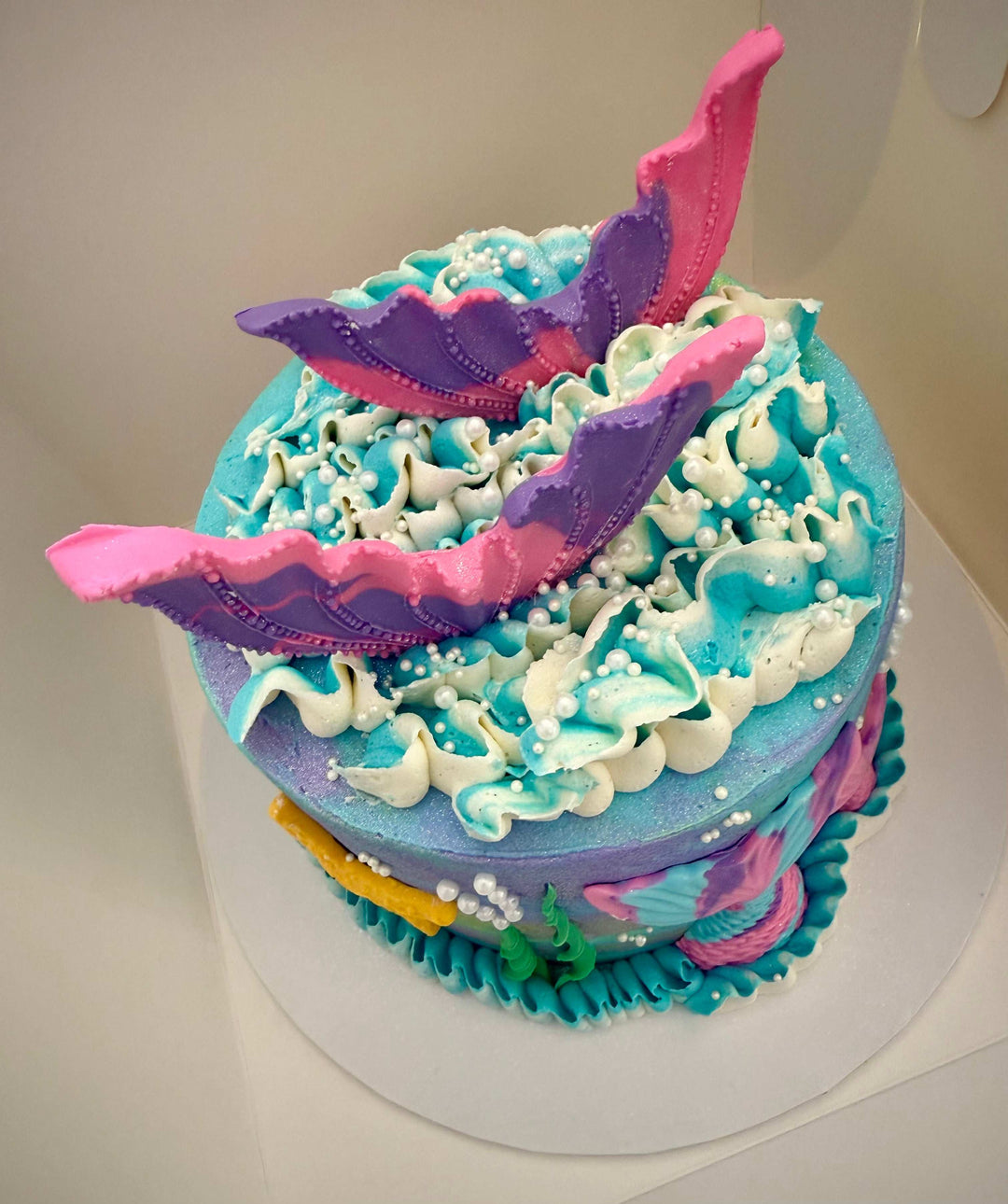 Colorful cake with mermaid-themed decorations on a white background