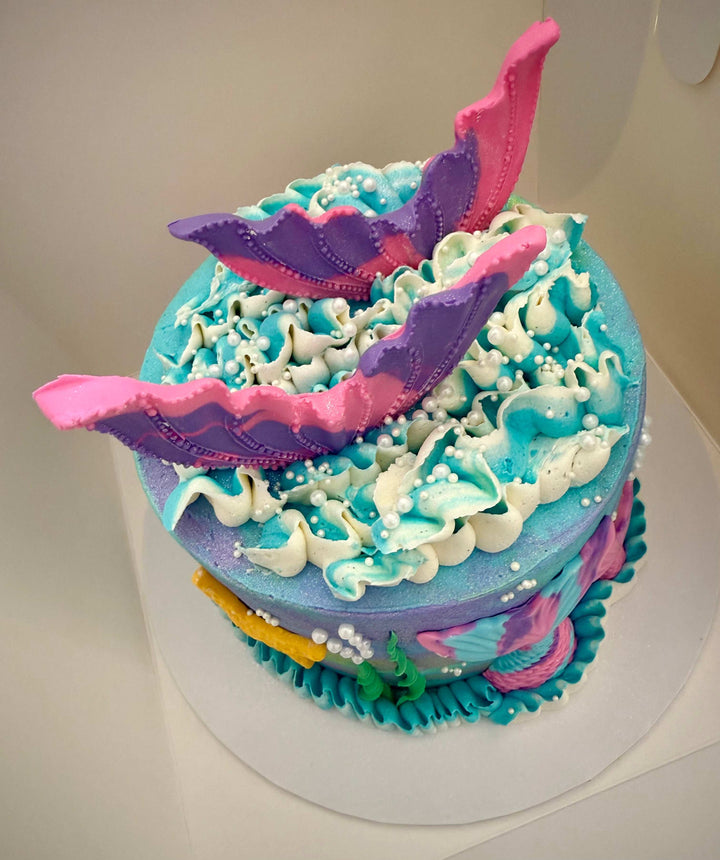 Colorful cake with mermaid-themed decorations on a white background