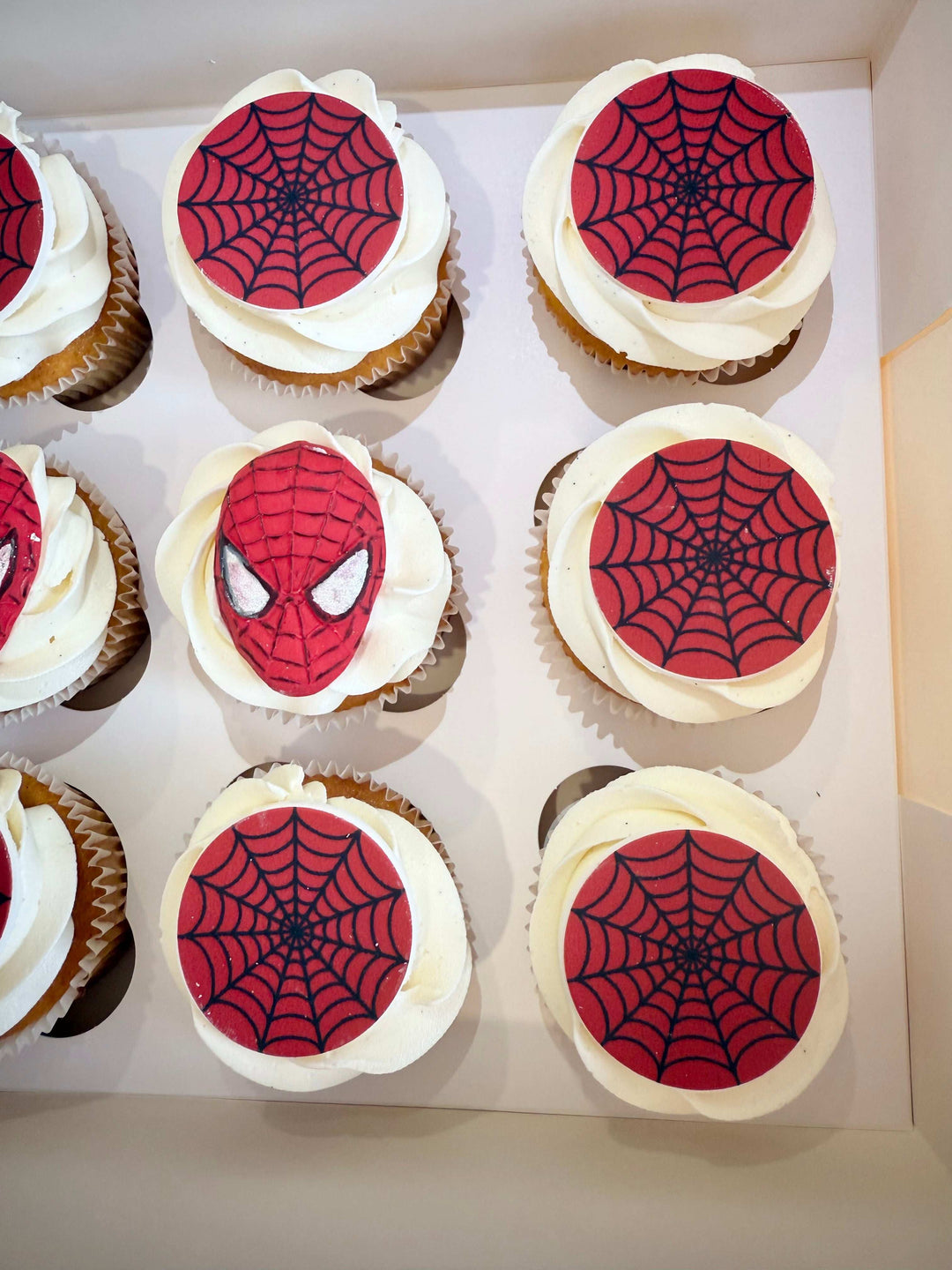 Cupcakes with Spider-Man face and web designs on white frosting