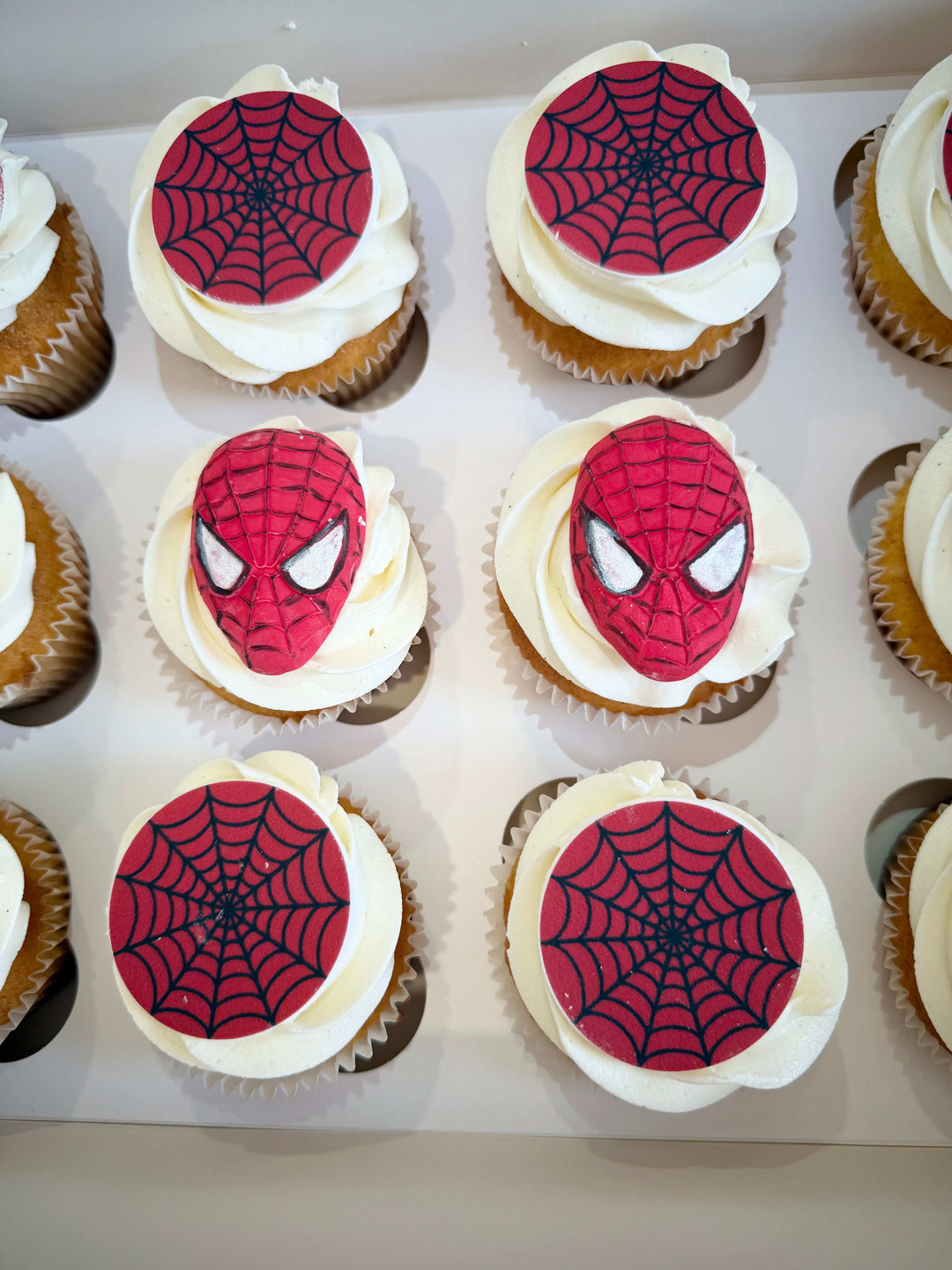 Cupcakes decorated with Spider-Man faces and web patterns on a white tray.