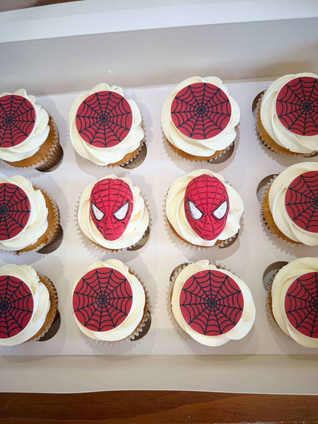 Spider-Man themed cupcakes with red and black spider designs on white frosting.